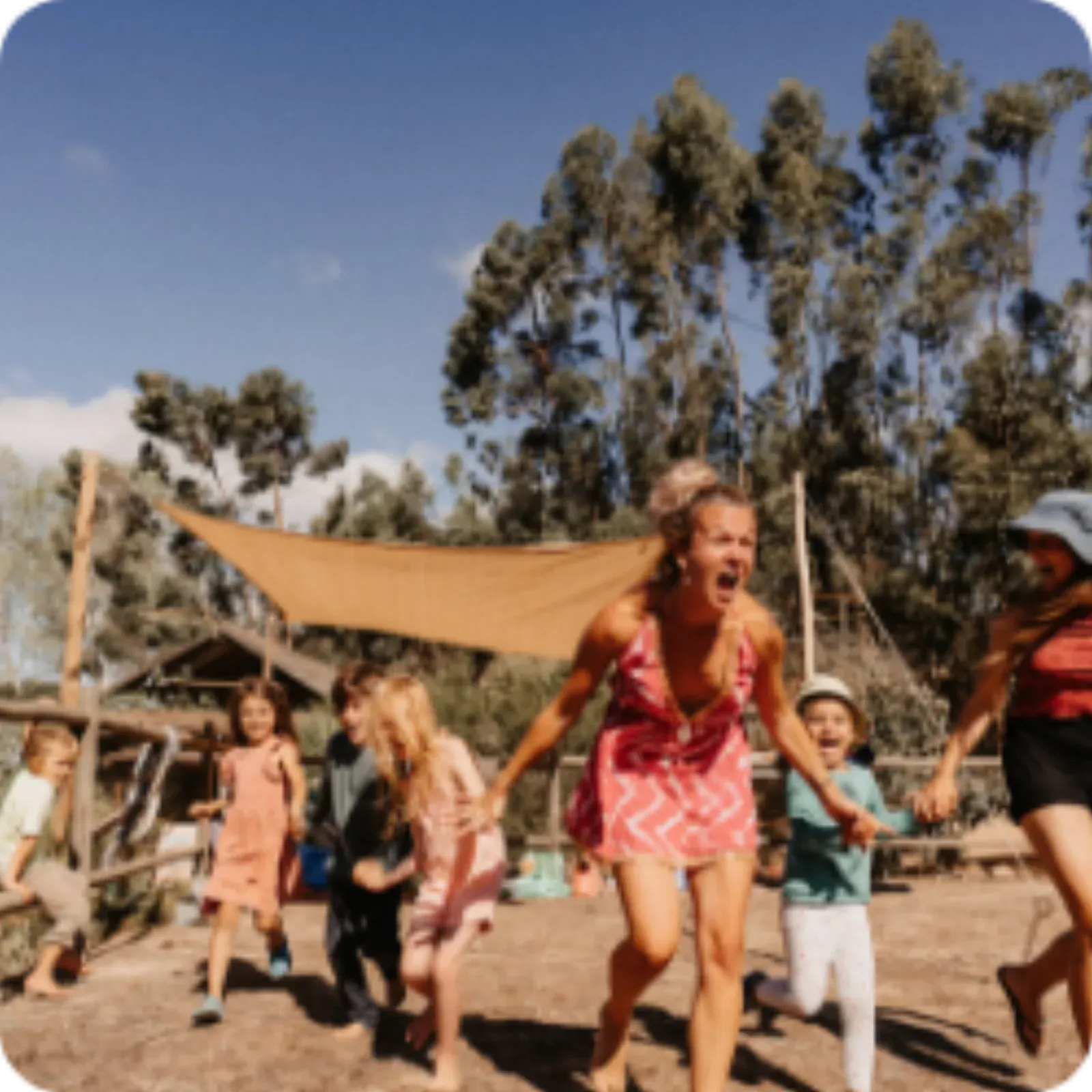 Families running and laughing under a sun sail between the trees