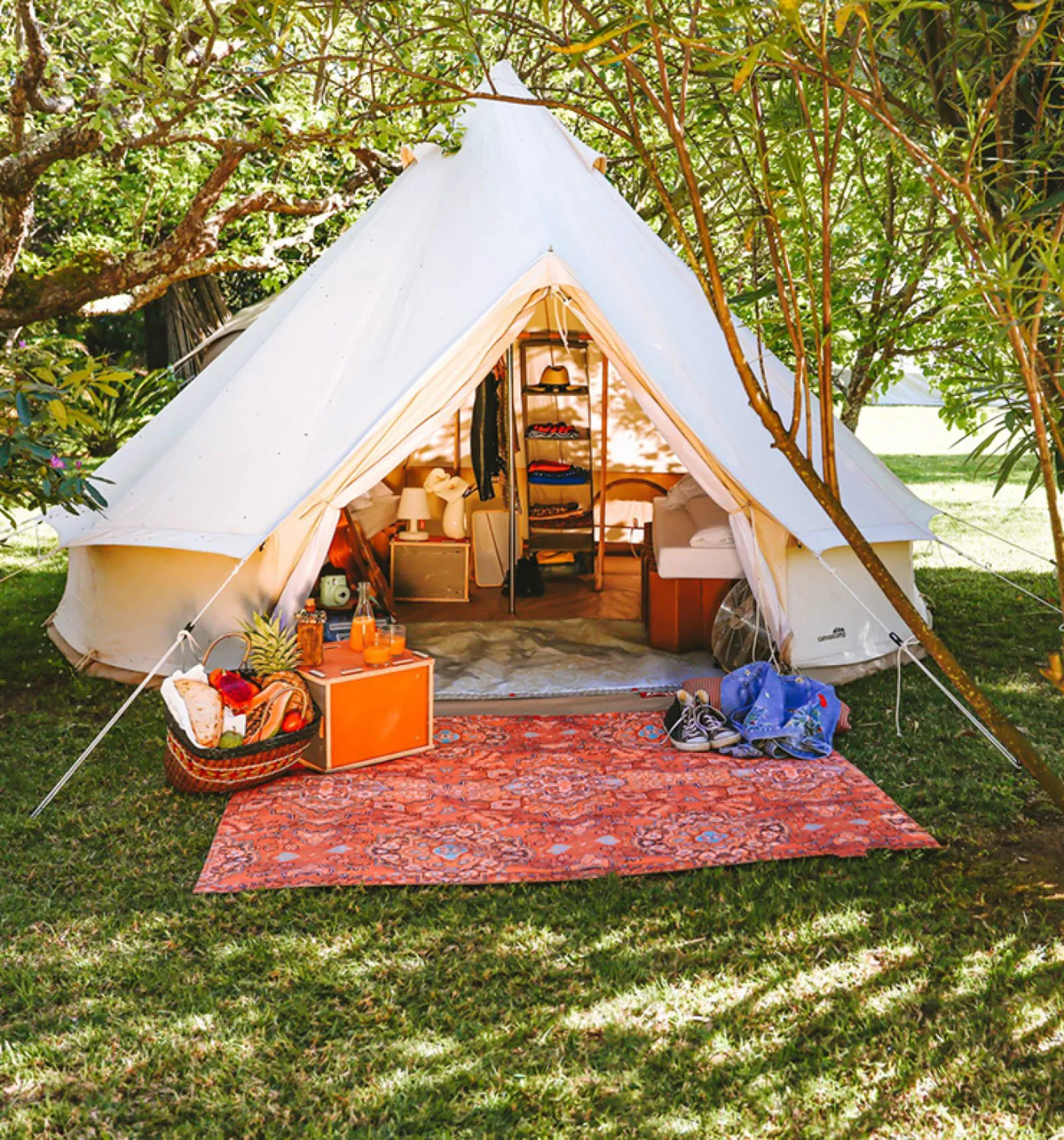A white bell tent set up under the trees with a rug outside